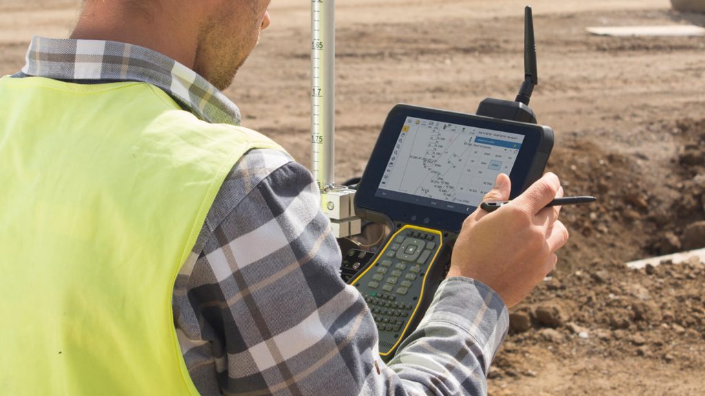 Surveyor using Machine Control Systems on a construction site, capturing and managing grading data with a field controller for improved earthmoving accuracy.